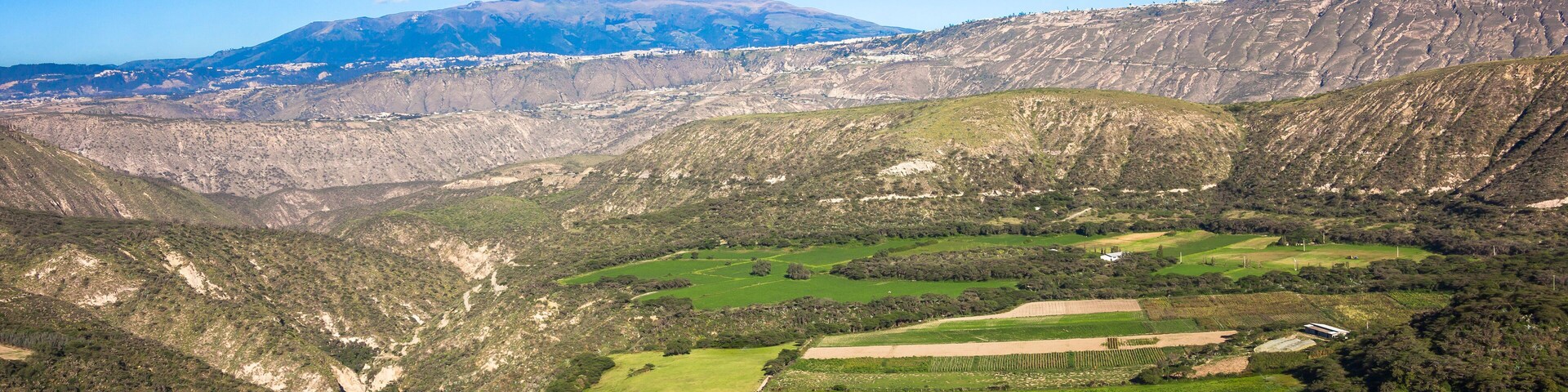 Un paisaje montañoso con campos verdes y una cadena montañosa distante.