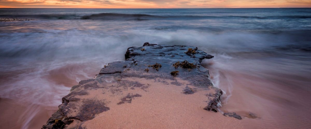 A rocky shoreline with waves at sunset.