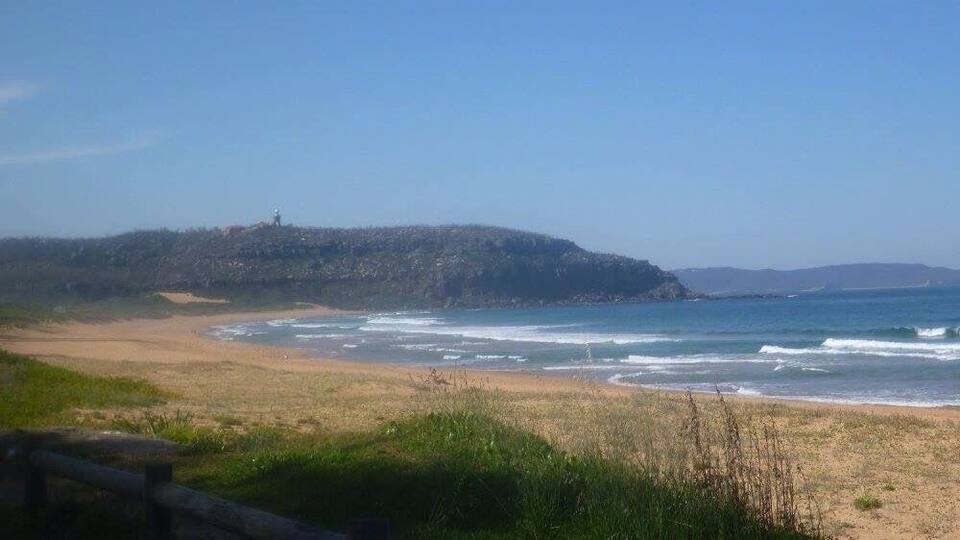 A beach with waves, a sandy shore, and a hill with a structure in the distance.