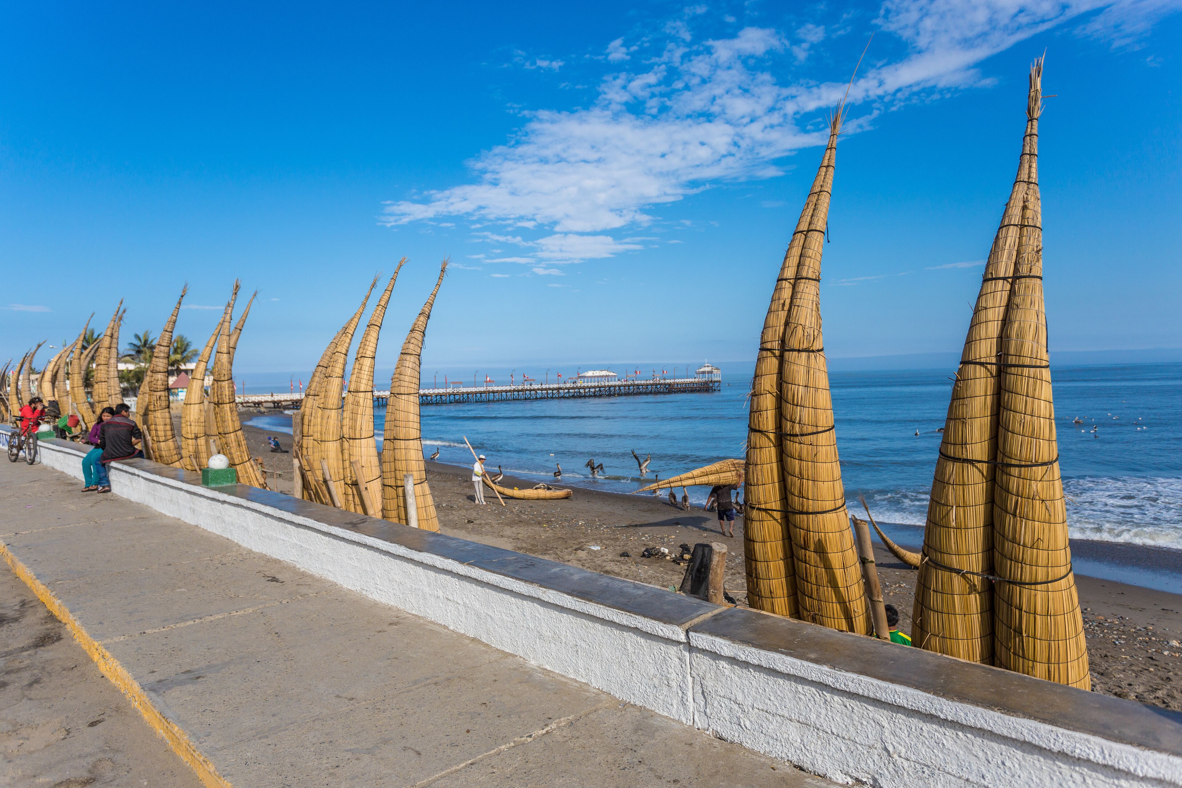 A beach with bamboo structures, a pier, and people in the background.