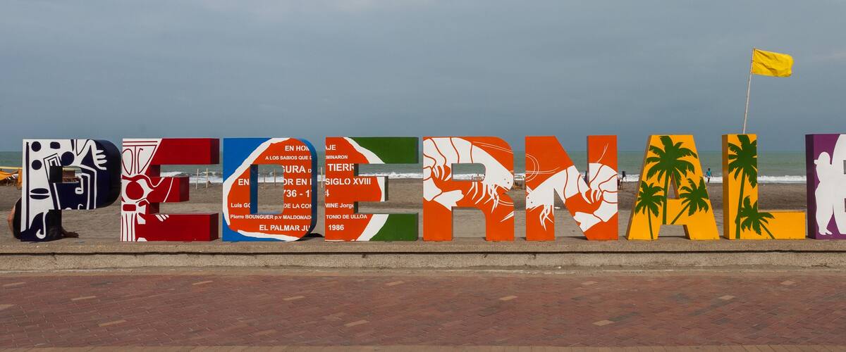 A colorful beachside installation spelling out "REGINAESTE" with palm tree and abstract designs.