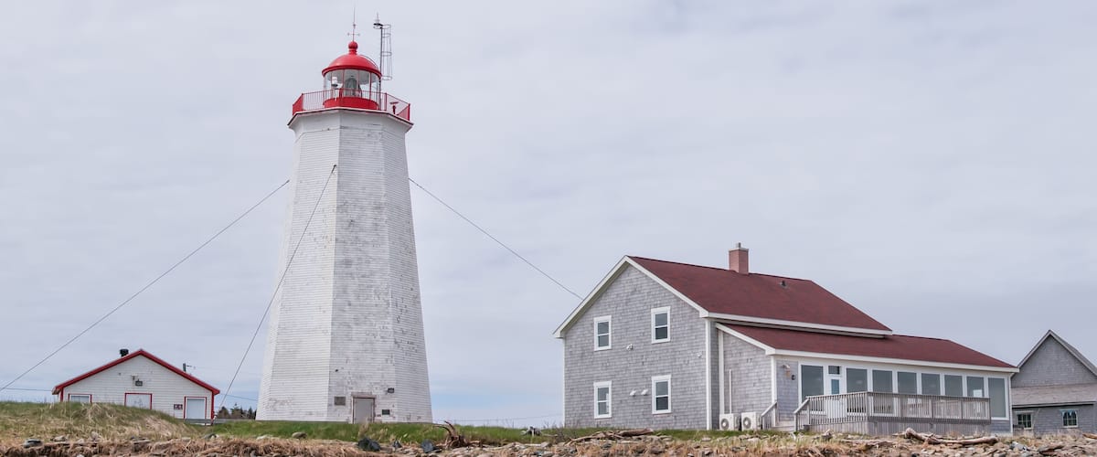 A white lighthouse with a red top, a small house with a red roof, and another house with a grey roof.