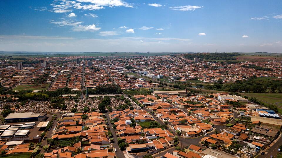 A cityscape with red-roofed buildings, green spaces, and a clear blue sky.