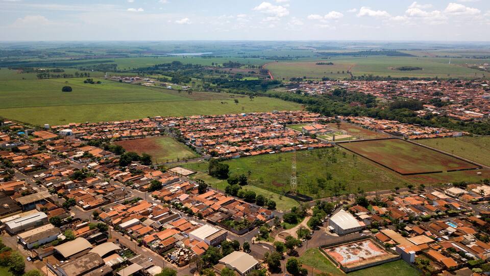 An aerial view of a town with red-roofed houses, green fields, and a large open area.