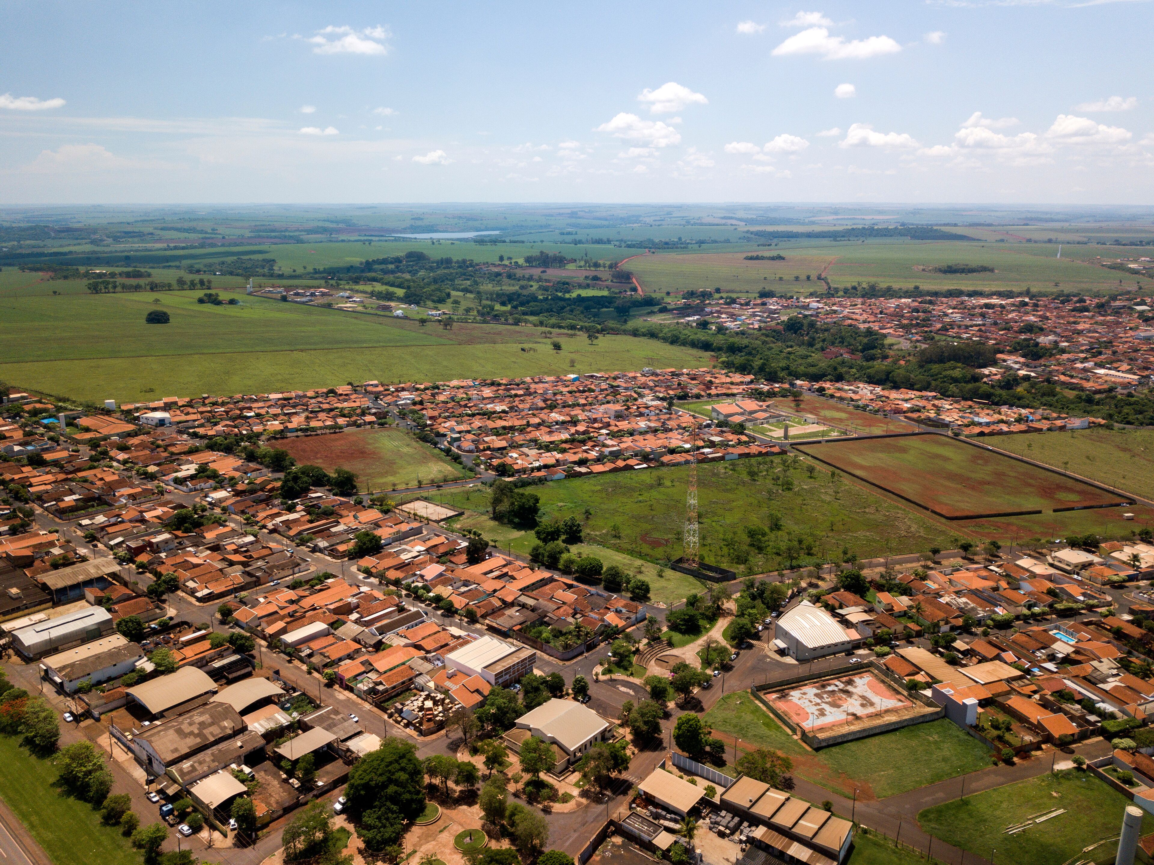 An aerial view of a town with red-roofed houses, green fields, and a large open area.