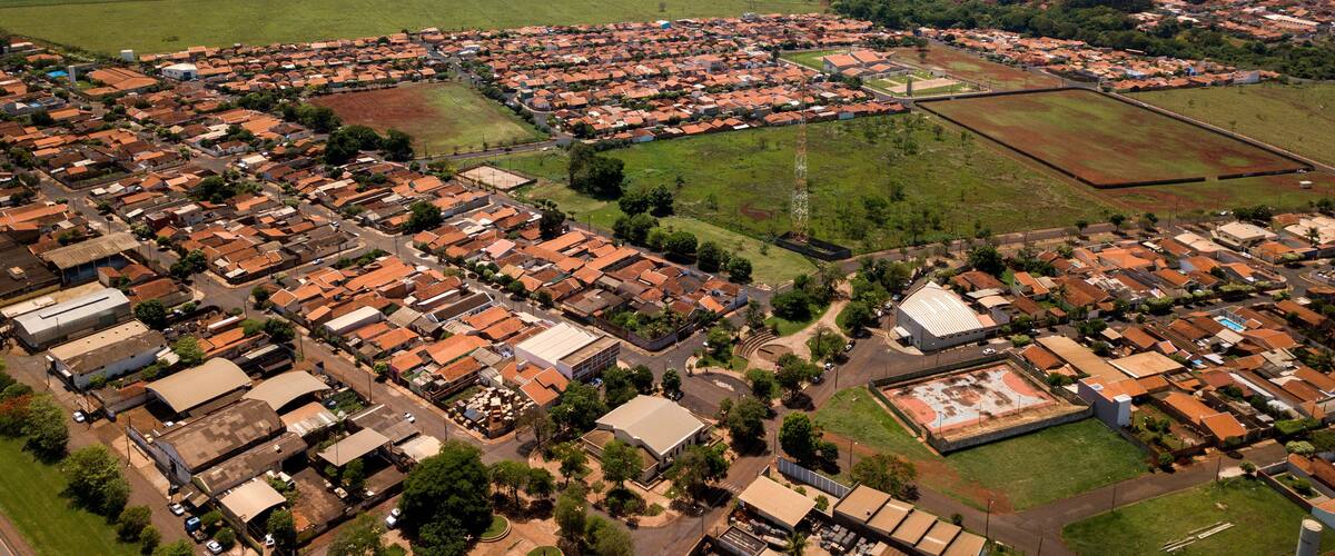An aerial view of a town with red-roofed houses, green fields, and a large open area.