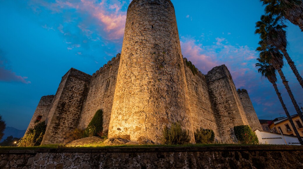 Eine historische Steinburg mit einem zentralen Turm, umgeben von Palmen und blauem Himmel.