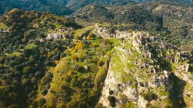 A mountainous landscape with ruins on a cliffside and a village in the valley below.