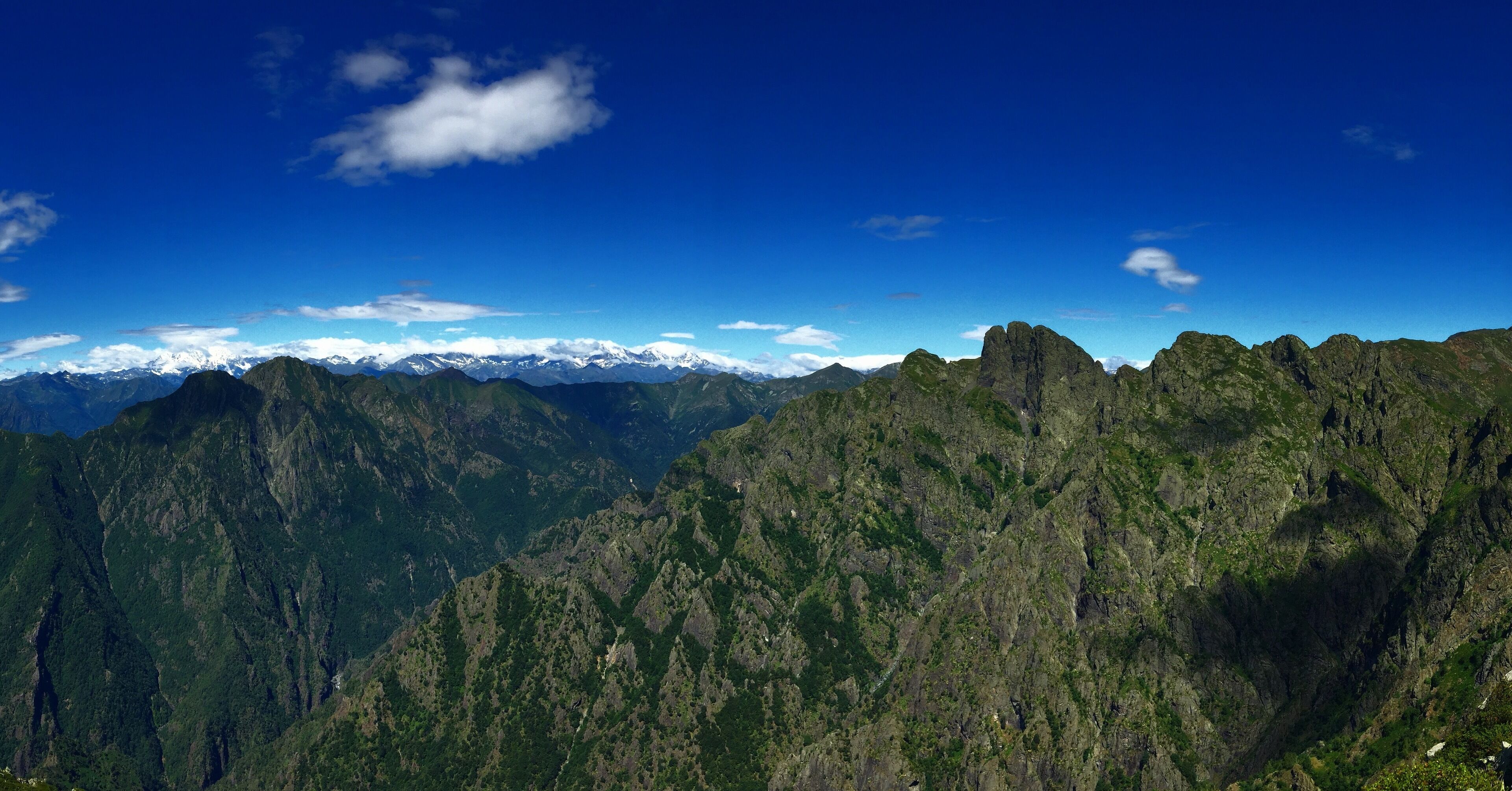 A mountain range with snow-capped peaks and lush green valleys under a clear blue sky.