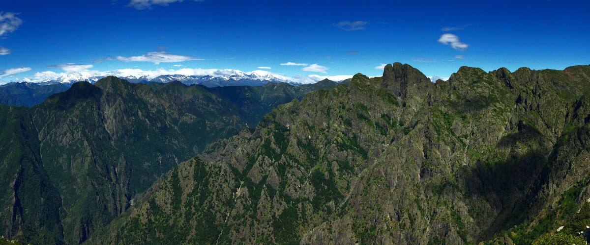 A mountain range with snow-capped peaks and lush green valleys under a clear blue sky.