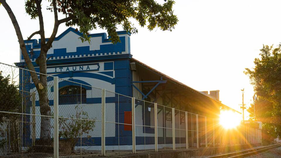 A train station with a blue and white facade, surrounded by gravel and tracks.
