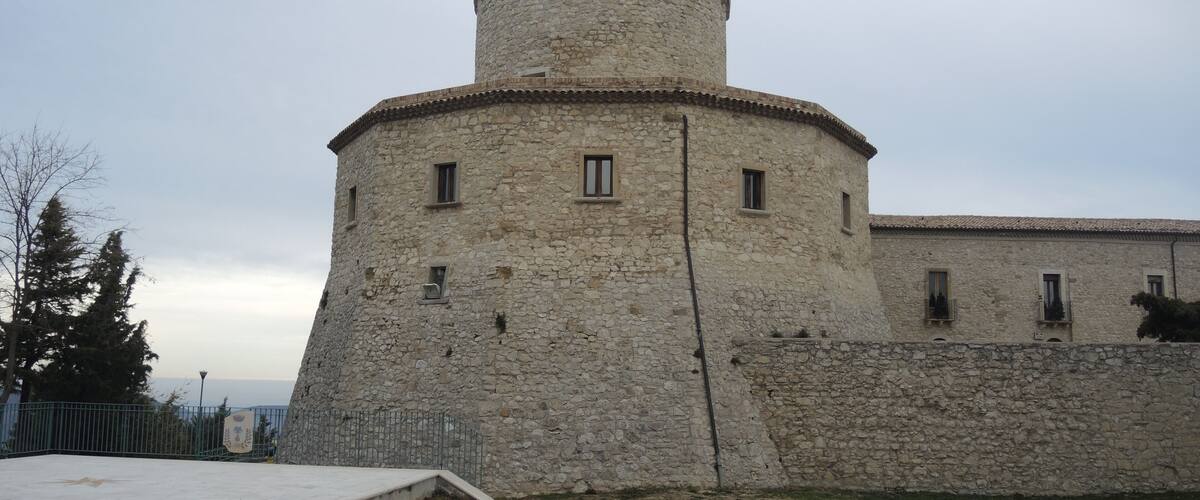 A stone castle with a round tower and a paved area in front.