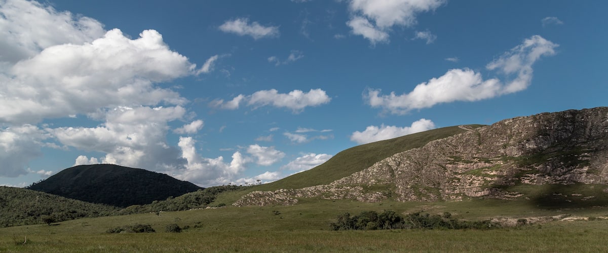 A grassy field with a rocky hill and a mountain in the background.