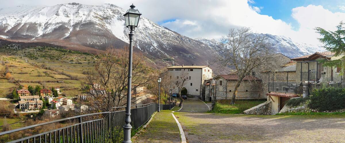 A village with snow-capped mountains in the background, a paved road, and traditional buildings.