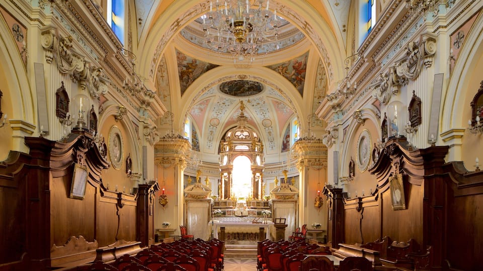 An ornate church interior with high ceilings, chandeliers, and red pews.