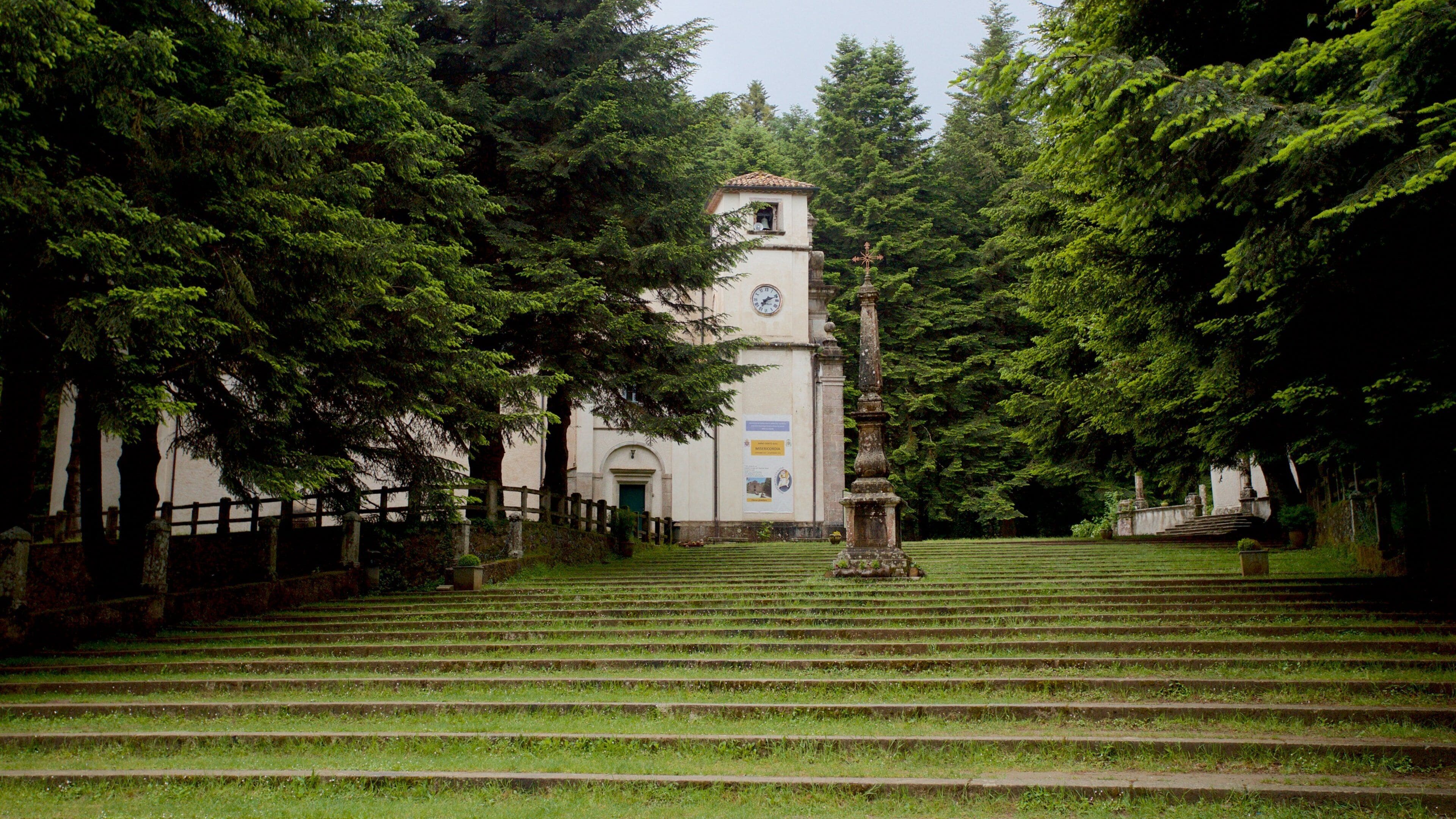 A church with a clock tower surrounded by lush green trees and a set of stairs leading up to it.