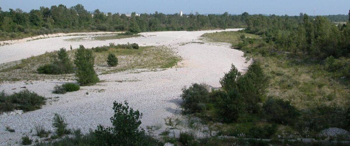 A river meandering through a landscape with sparse vegetation and distant trees.