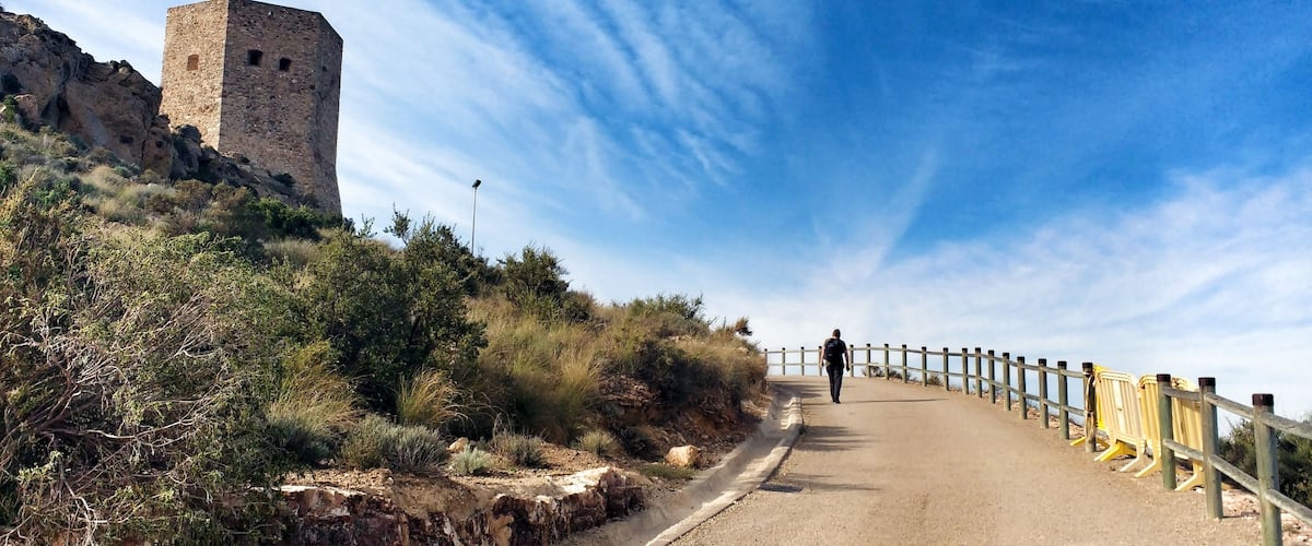 A pathway leading to a stone tower on a hill, with a clear sky and sparse vegetation.