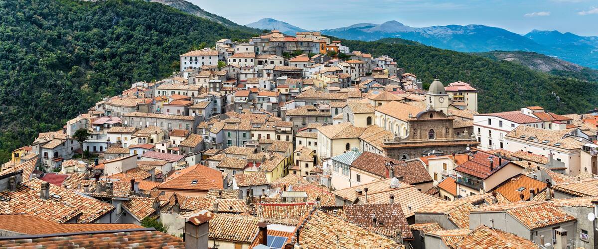 A town built on a hillside with terracotta roofs and surrounded by mountains.