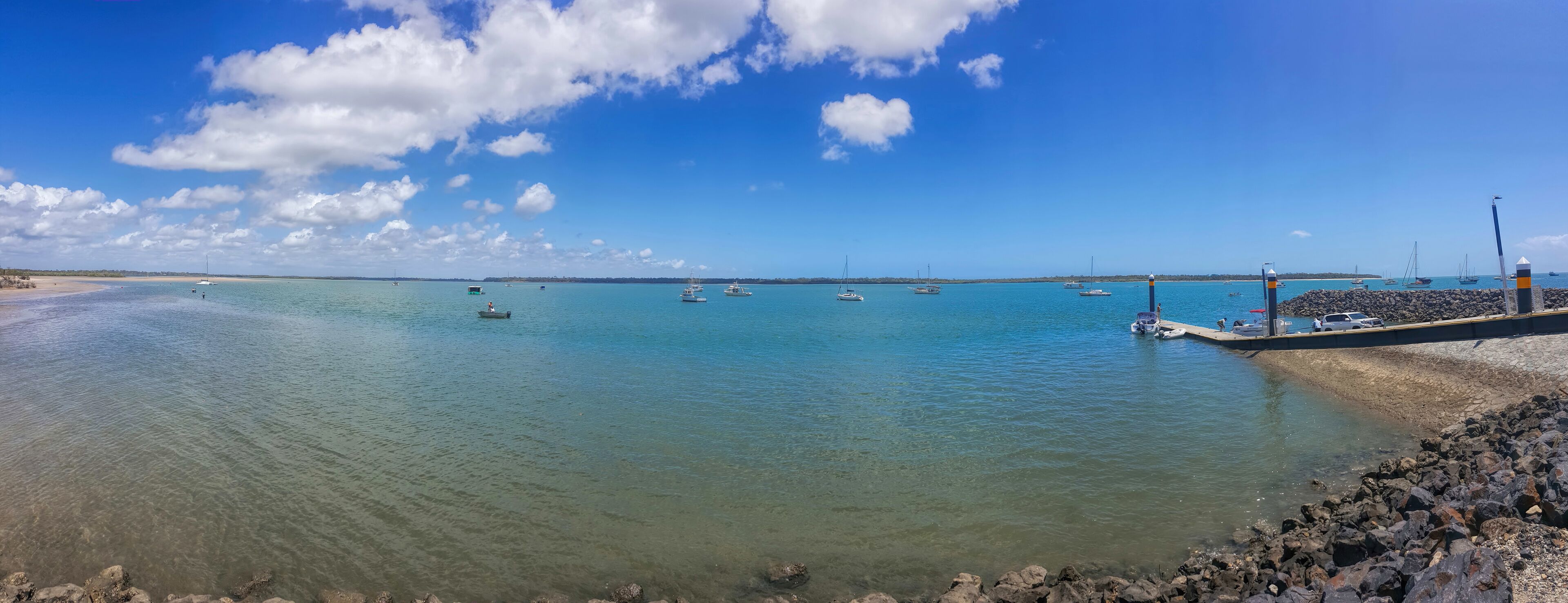 A coastal scene with calm waters, boats, and a rocky breakwater.
