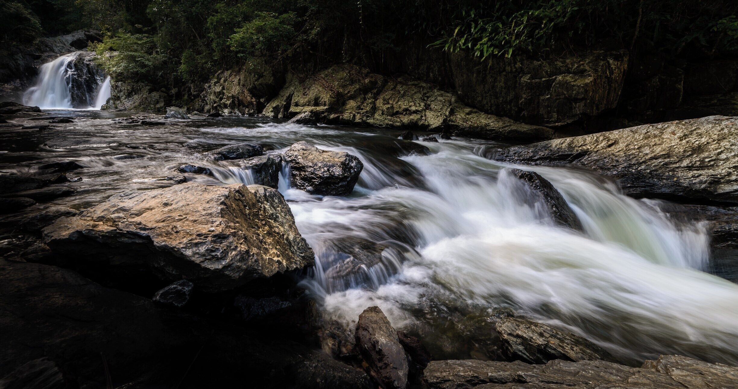 A river flowing over rocks with a waterfall in the background.