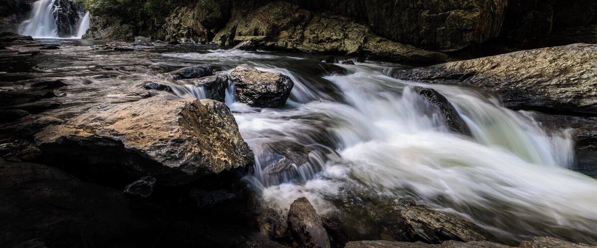 A river flowing over rocks with a waterfall in the background.