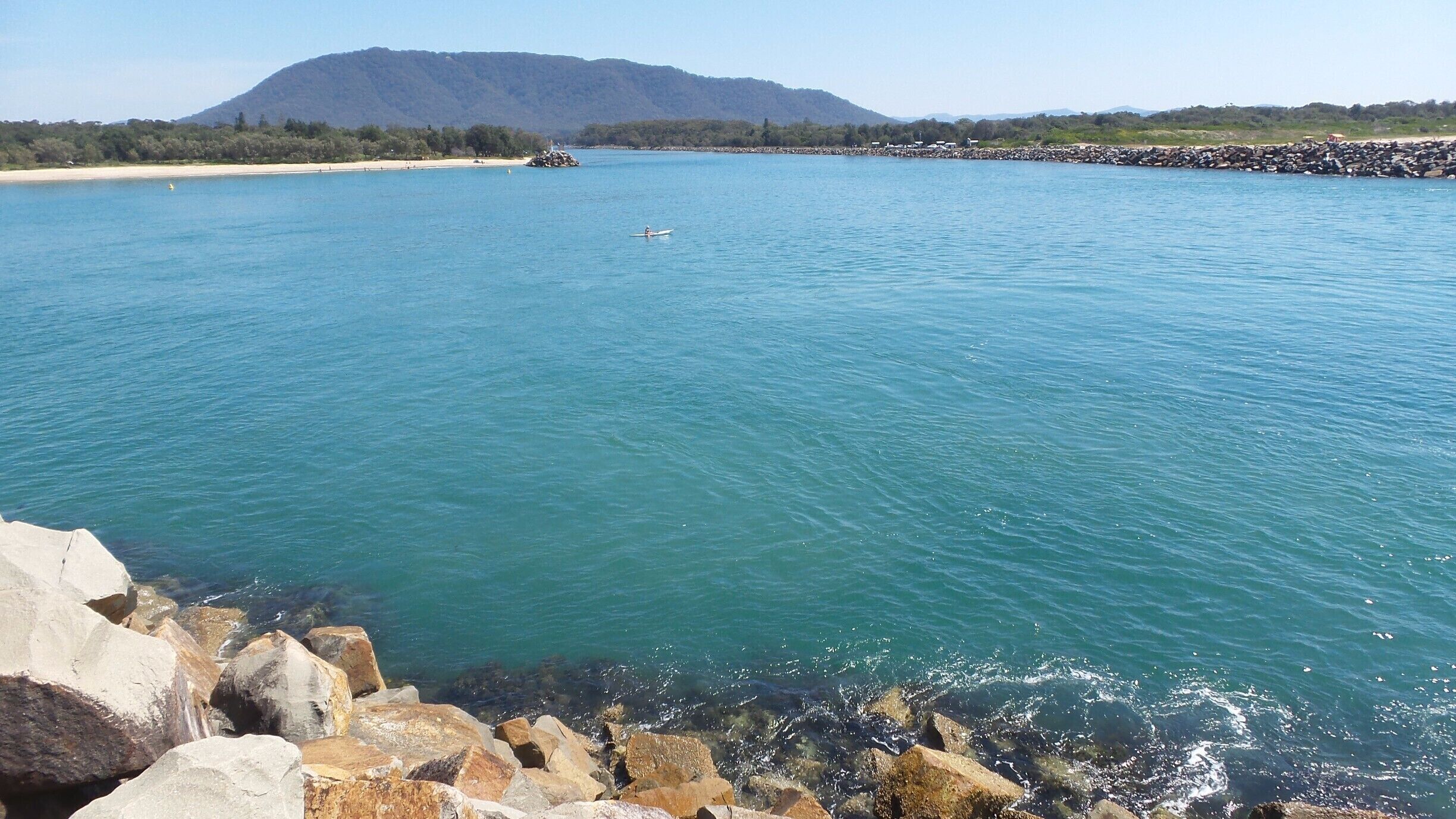 A calm lake with clear blue water, surrounded by rocky shores and a distant mountain range.