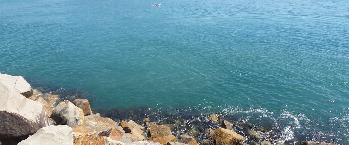 A calm lake with clear blue water, surrounded by rocky shores and a distant mountain range.