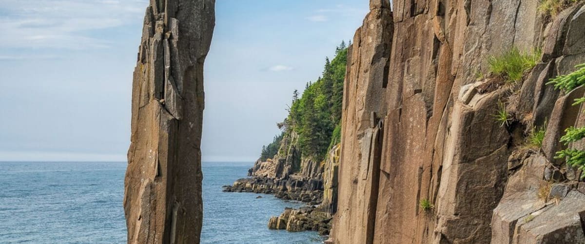 A coastal rock formation with a prominent vertical rock structure and layered cliffs.