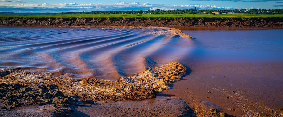 A river with a rocky shoreline and a distant green landscape.