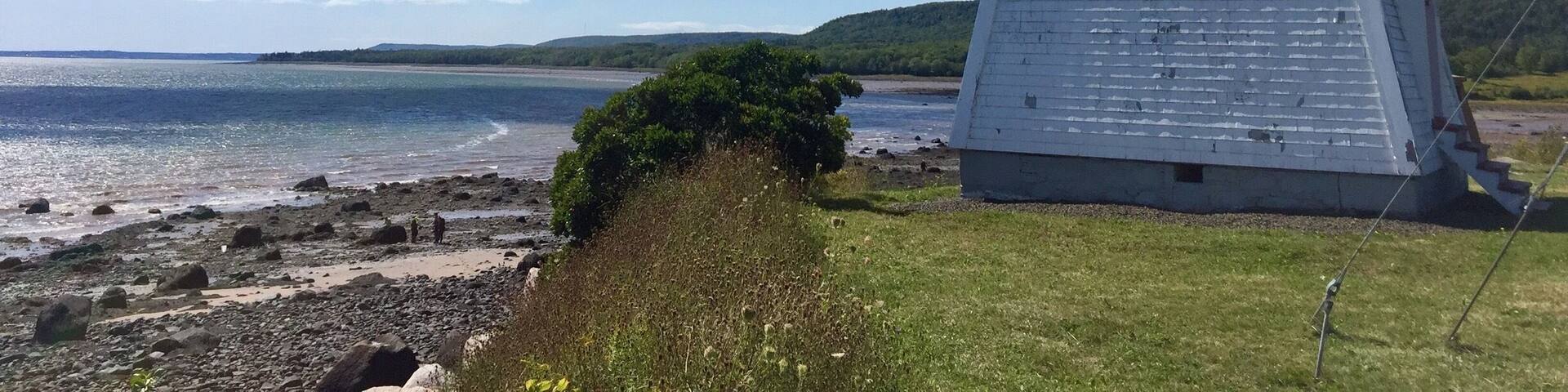A white lighthouse with a red top by a rocky shoreline.