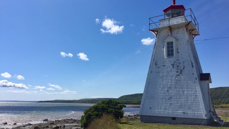A white lighthouse with a red top by a rocky shoreline.