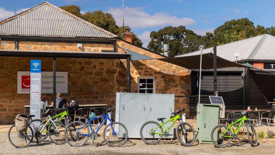 A stone building with a corrugated metal roof, bicycles parked in front, and a sign indicating free Wi-Fi.