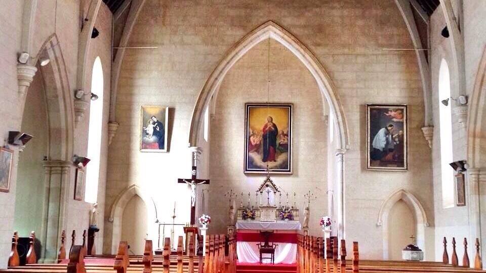 A church interior with a red carpet aisle, wooden pews, and religious paintings on the walls.