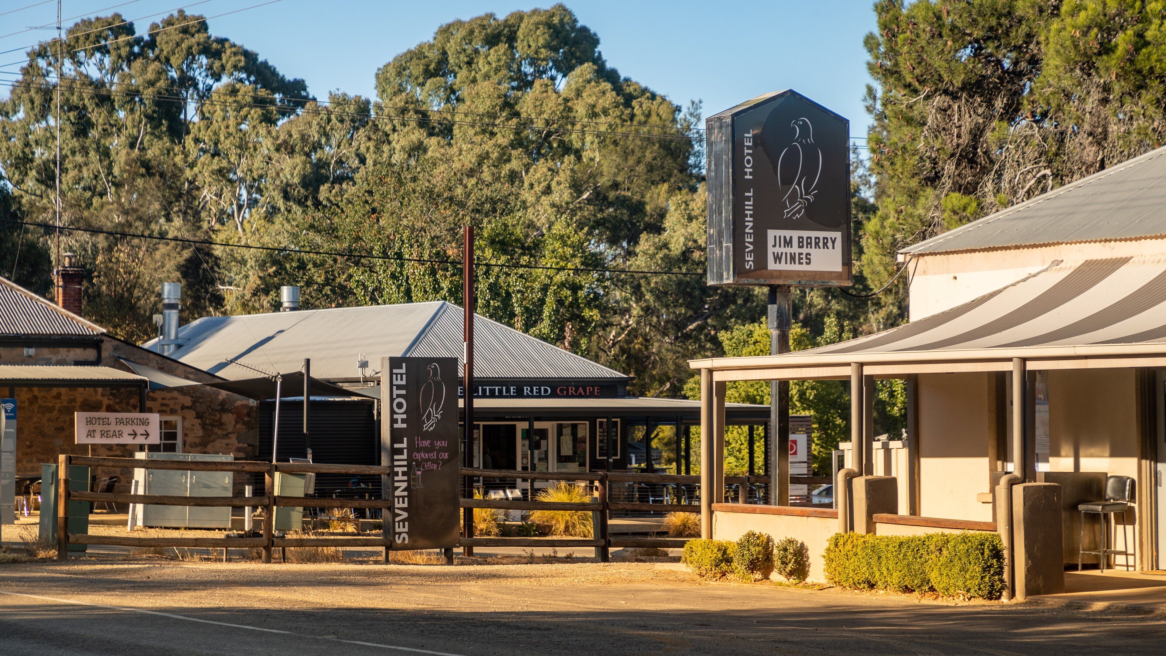 A roadside with a hotel named 'SEVENHILL HOTEL' and 'JIM BARRY WINES'. There is a sign for 'HOTEL PARKING AT REAR' and a building with a sign 'LITTLE RED GRAPE'.