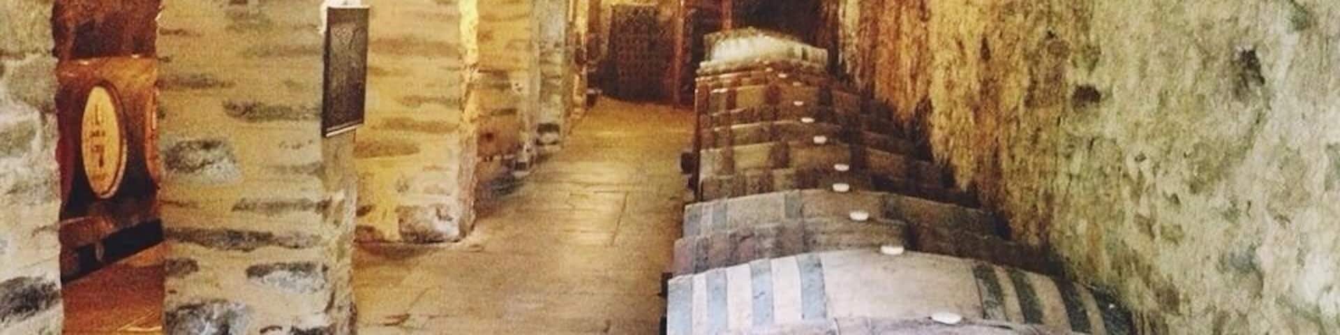 A stone-walled cellar with wooden barrels and a staircase leading down.