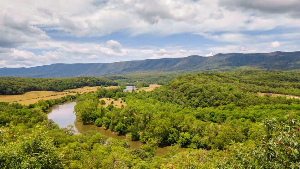 A river winding through a lush valley with dense greenery and distant mountains under a partly cloudy sky.