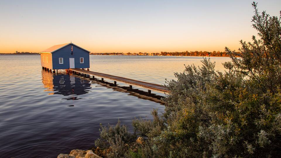 A blue house on stilts by a calm lake with a wooden dock extending into the water.