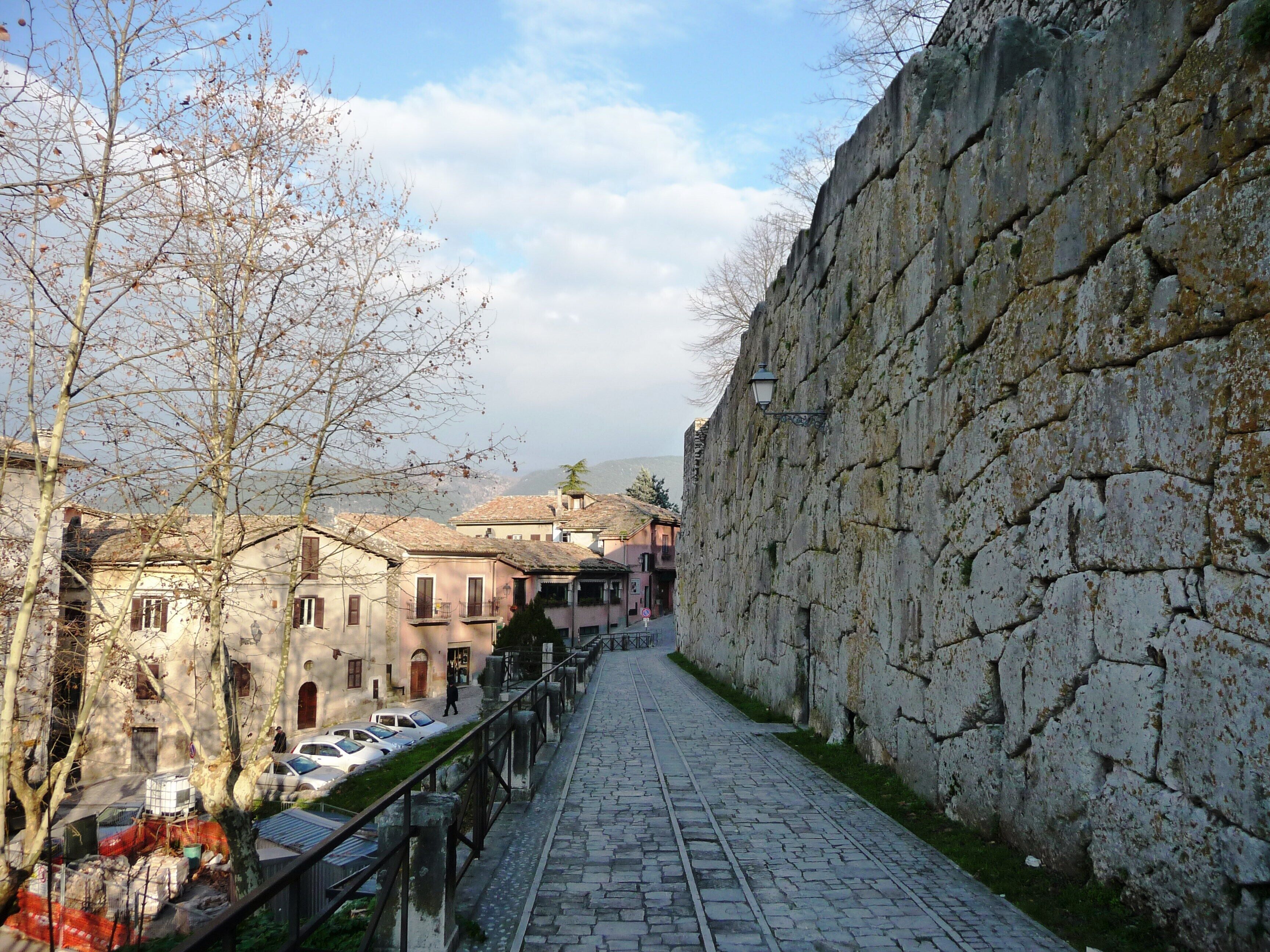 A cobblestone street flanked by historic stone walls and buildings.