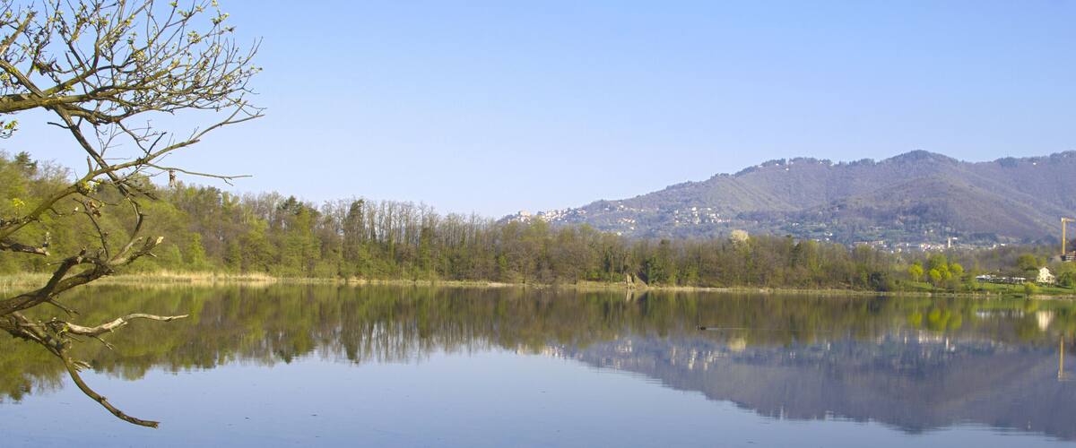 A calm lake with reflections of trees and mountains in the background.