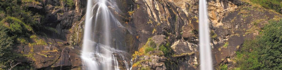 Ein mehrstufiger Wasserfall stürzt über eine felsige Klippe, umgeben von üppigem Grün.