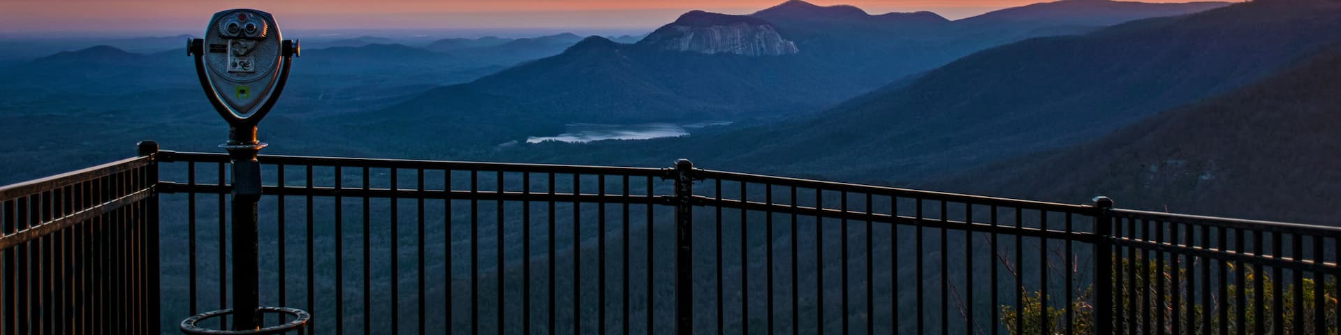 A panoramic view of a mountainous landscape with a telescope on a viewing platform.