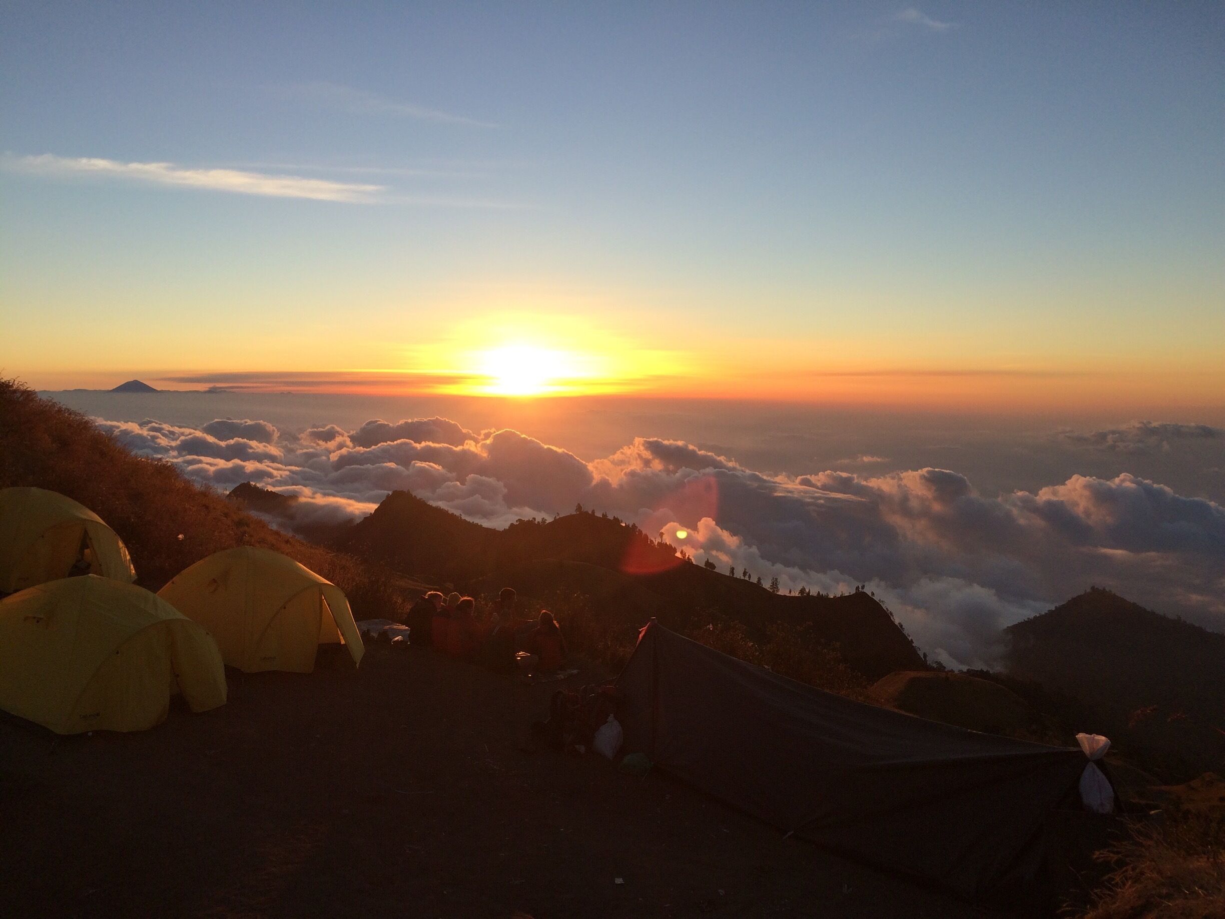 A sunrise over a mountain range with tents set up on the side.