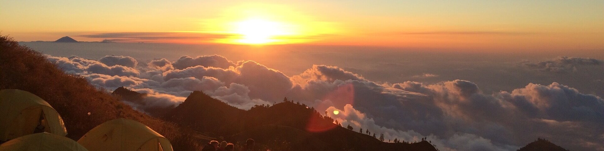 A sunrise over a mountain range with tents set up on the side.