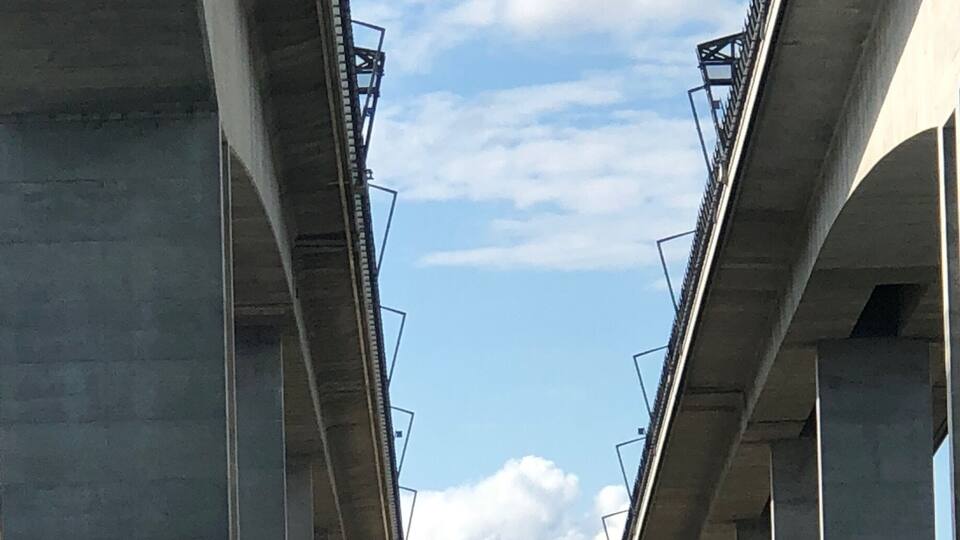 Eine Betonbrücke überspannt einen Fluss unter einem wolkenlosen Himmel.
