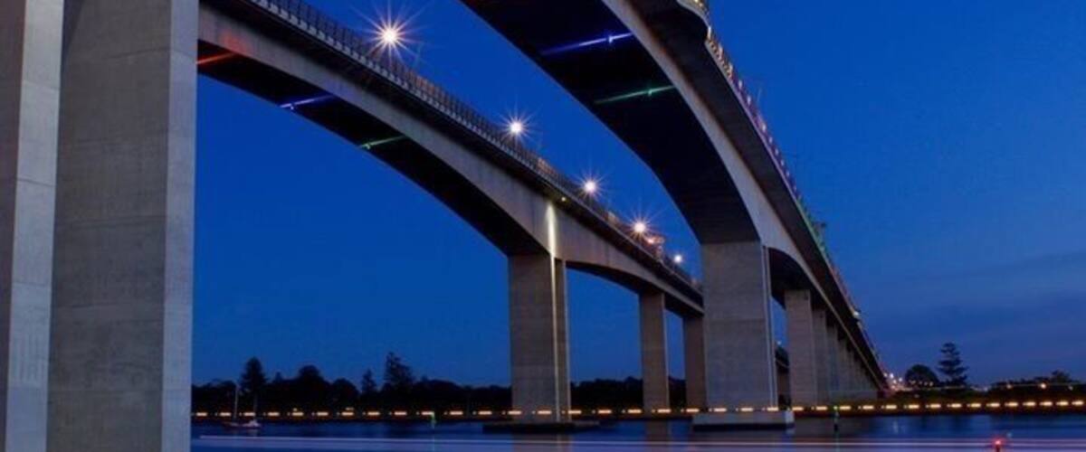A multi-level bridge at dusk with lights reflecting on the water.