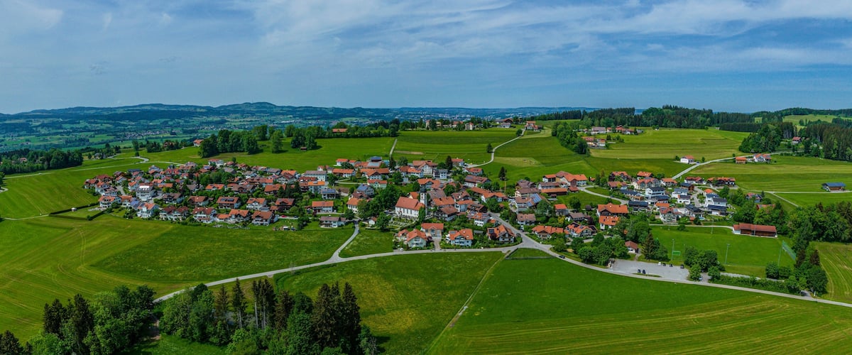A rural village with red-roofed houses, green fields, and a winding road.