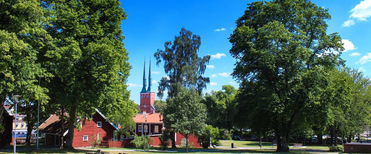A red church with a tall steeple, surrounded by lush green trees and a well-maintained lawn.