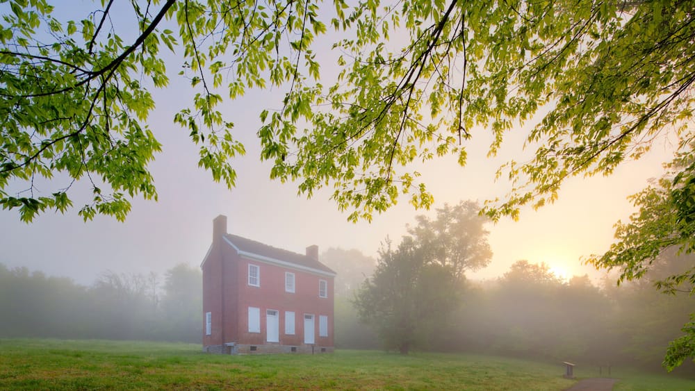 A red brick house surrounded by a foggy field with a path leading to a gazebo.