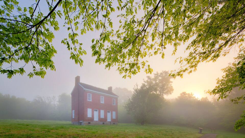 A red brick house surrounded by a foggy field with a path leading to a gazebo.